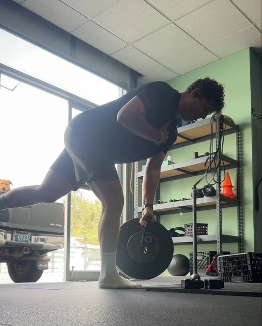 A man performing a cable row exercise at a gym, using a weight plate and resistance bands, with gym equipment and a large window in the background.