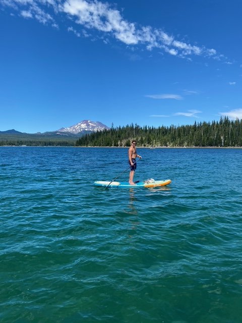 A man paddleboarding on a lake with a mountain in the background and a clear blue sky.