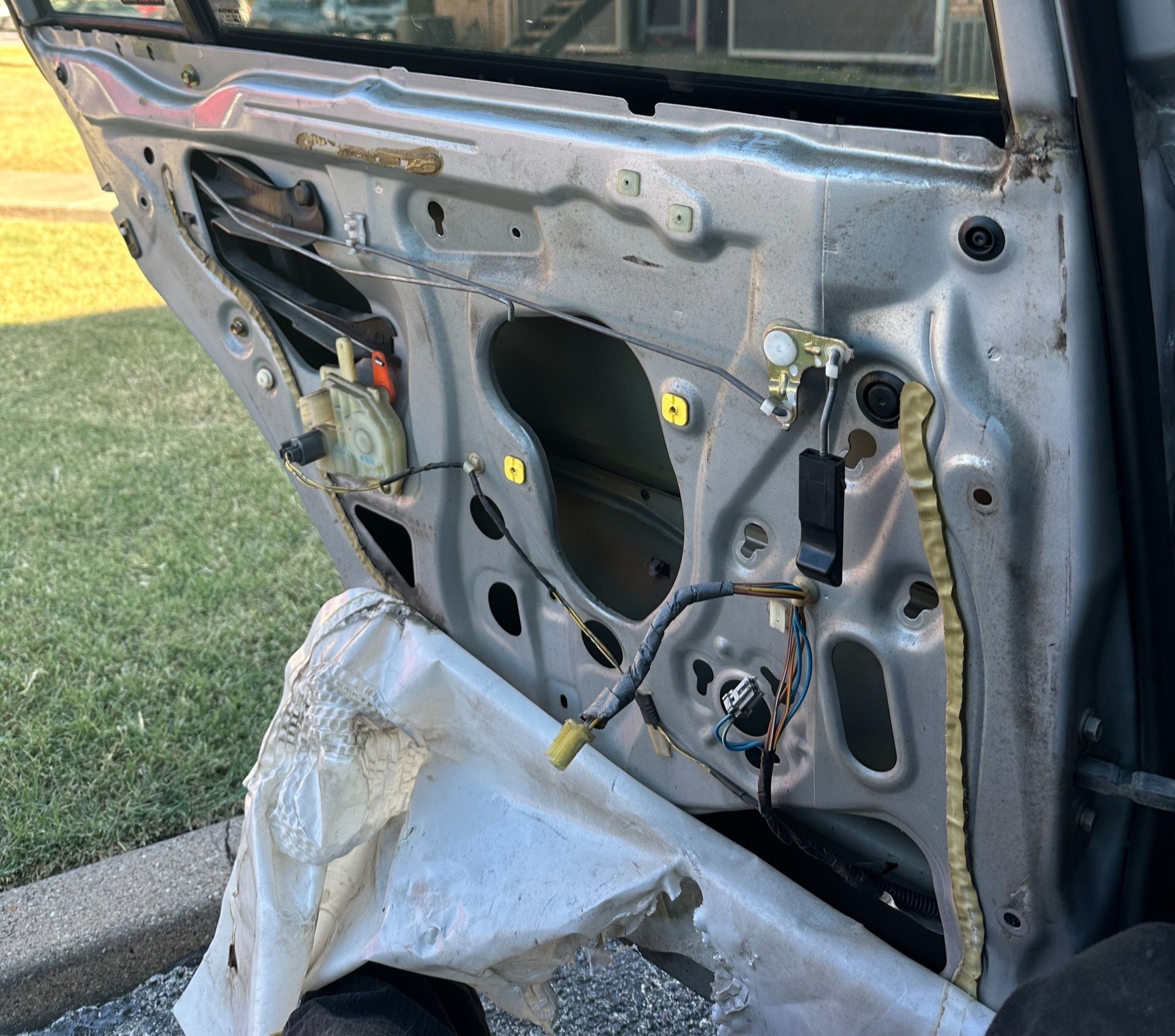 The interior door panel of a car with the panel removed, showing the metal structure, wiring, and mechanical components.