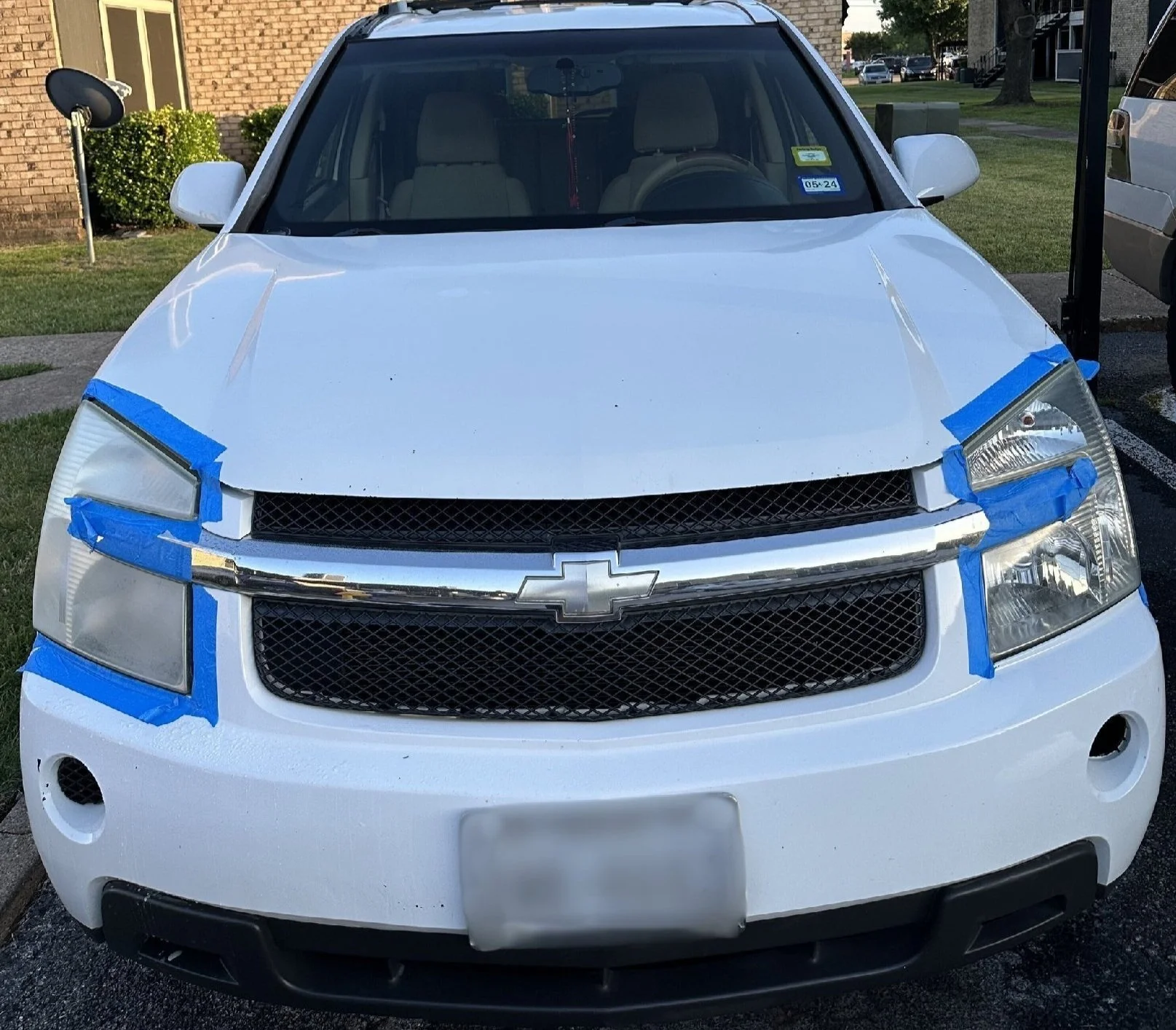 Front view of a white Chevrolet SUV with the hood taped off with blue painter's tape, likely for repairs or painting.
