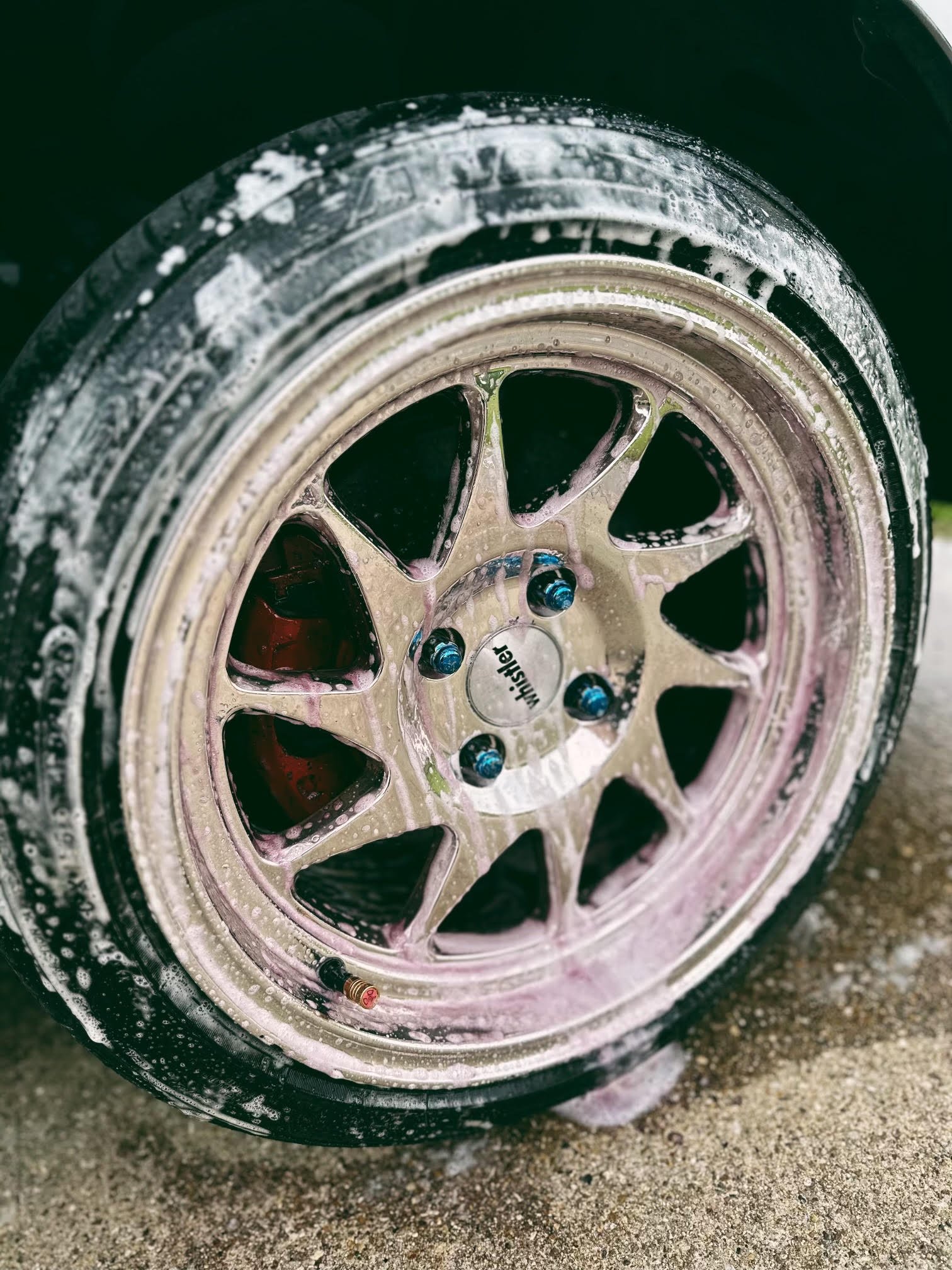 Close-up of a car wheel being cleaned with soap and foam, with soap bubbles on the tire and rim.
