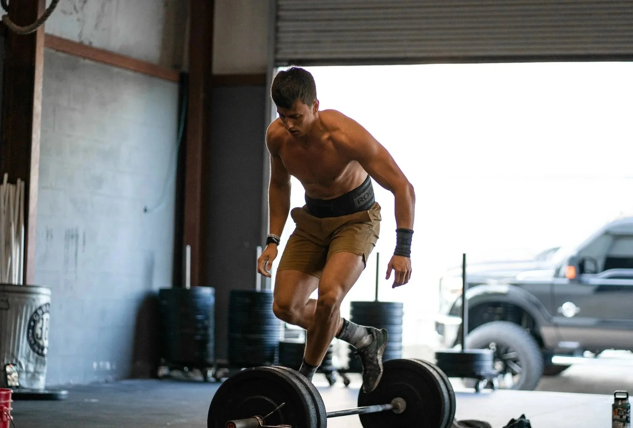 A man providing medical assistance to a woman lying on a therapy table in a gym. The woman appears to be in pain or discomfort, clutching her side. Gym equipment is visible in the background.