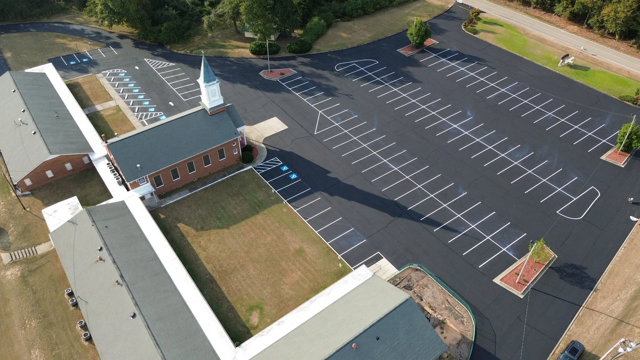 A church with an adjacent parking lot. The parking lot has designated spaces for disabled parking, a basketball court, and several trees.