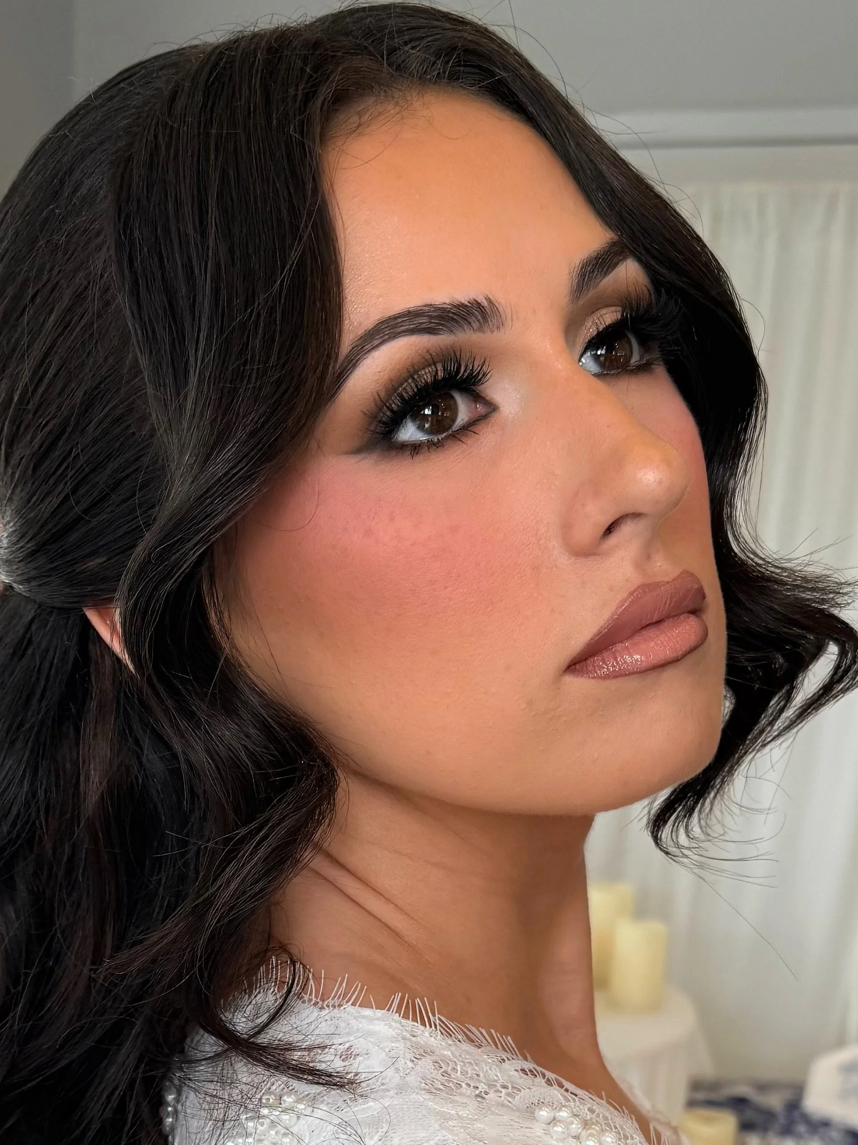 A woman with dark hair and makeup, wearing a white dress with pearl embellishments.