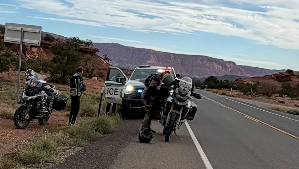 Two motorcycles pulled over on a desert highway in front of a ranger truck with its lights on