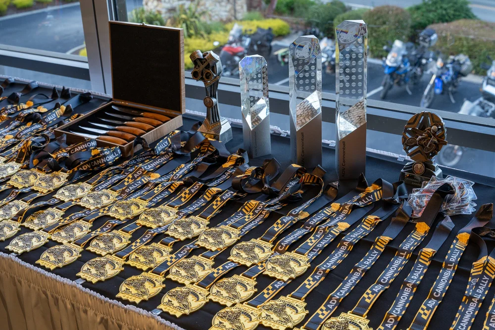 Rows of finisher's medals, glass trophies and a boxed set of steak knives laid out on a table