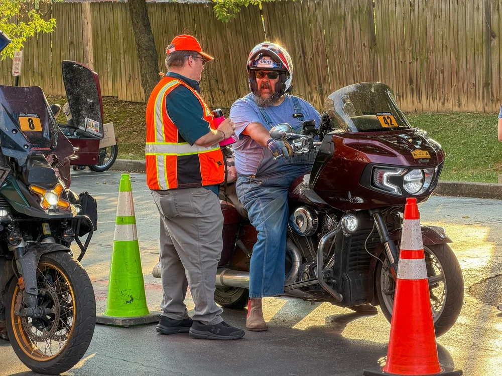 Jay Maher in overalls on his Indian bagger at the start line, talking to a starter