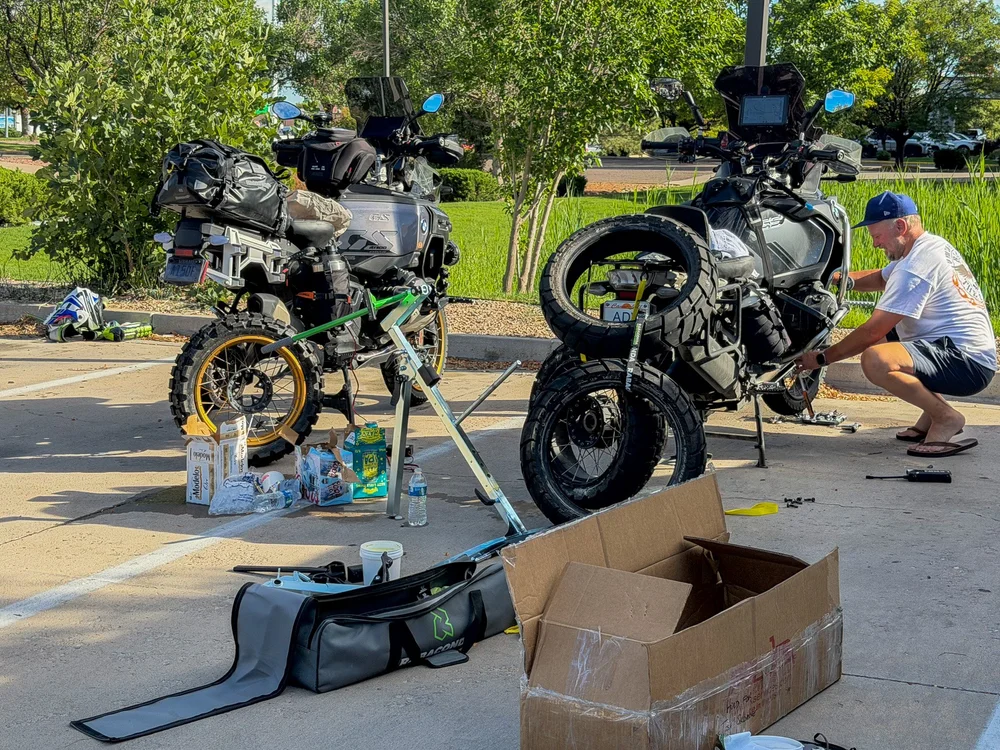 Two adventure motorcycles on stands in a parking lot with wheels off and new tires waiting