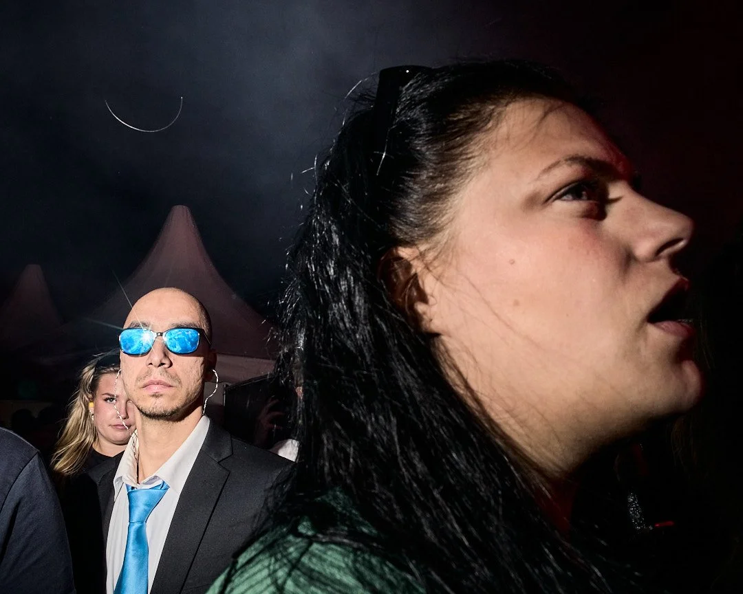 Close-up of a woman with black hair and a man with sunglasses, in a dark environment with tents in the background.