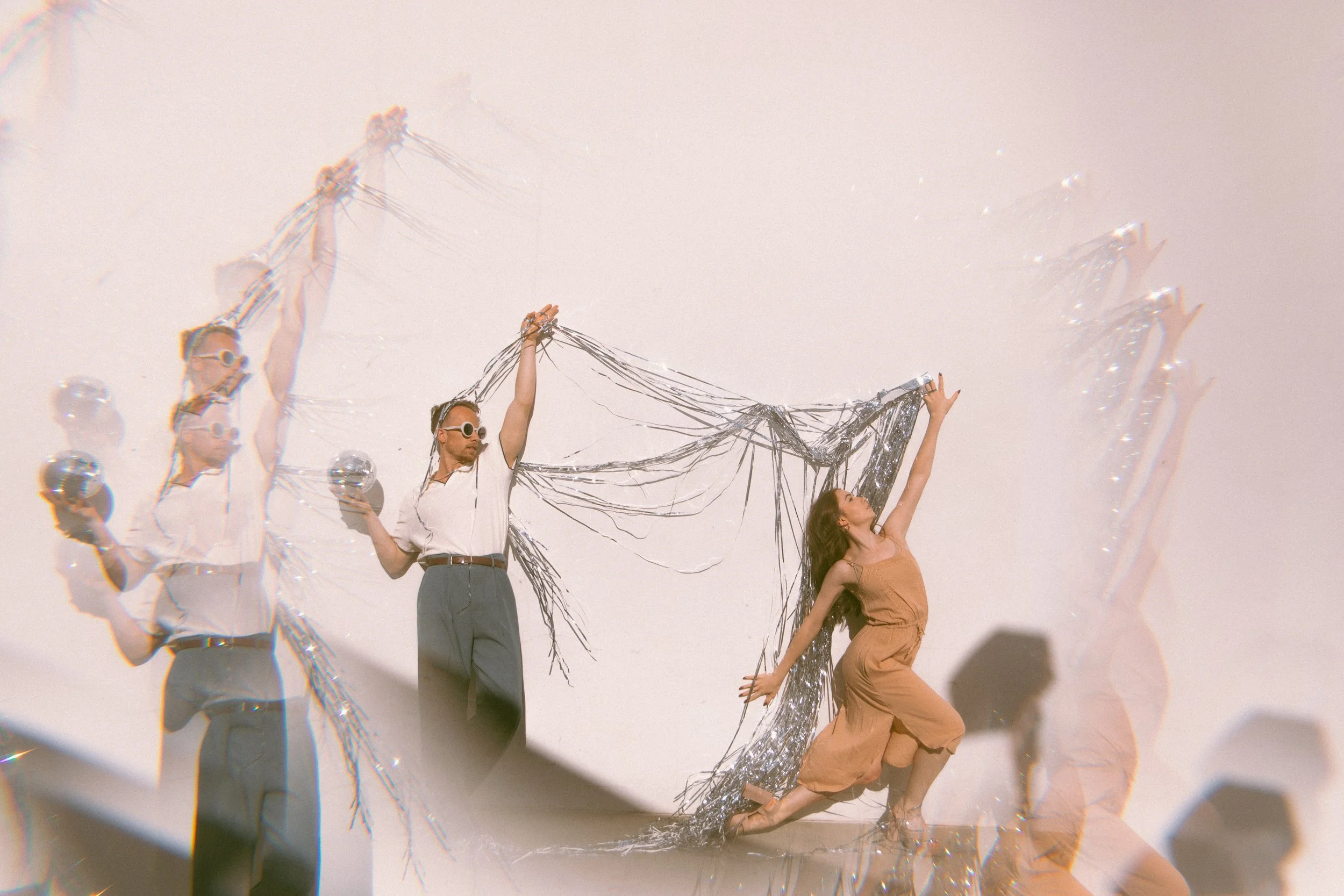 Dancers pose elegantly, suspending silver tinsel between them with a kaleidoscope lens effect.
