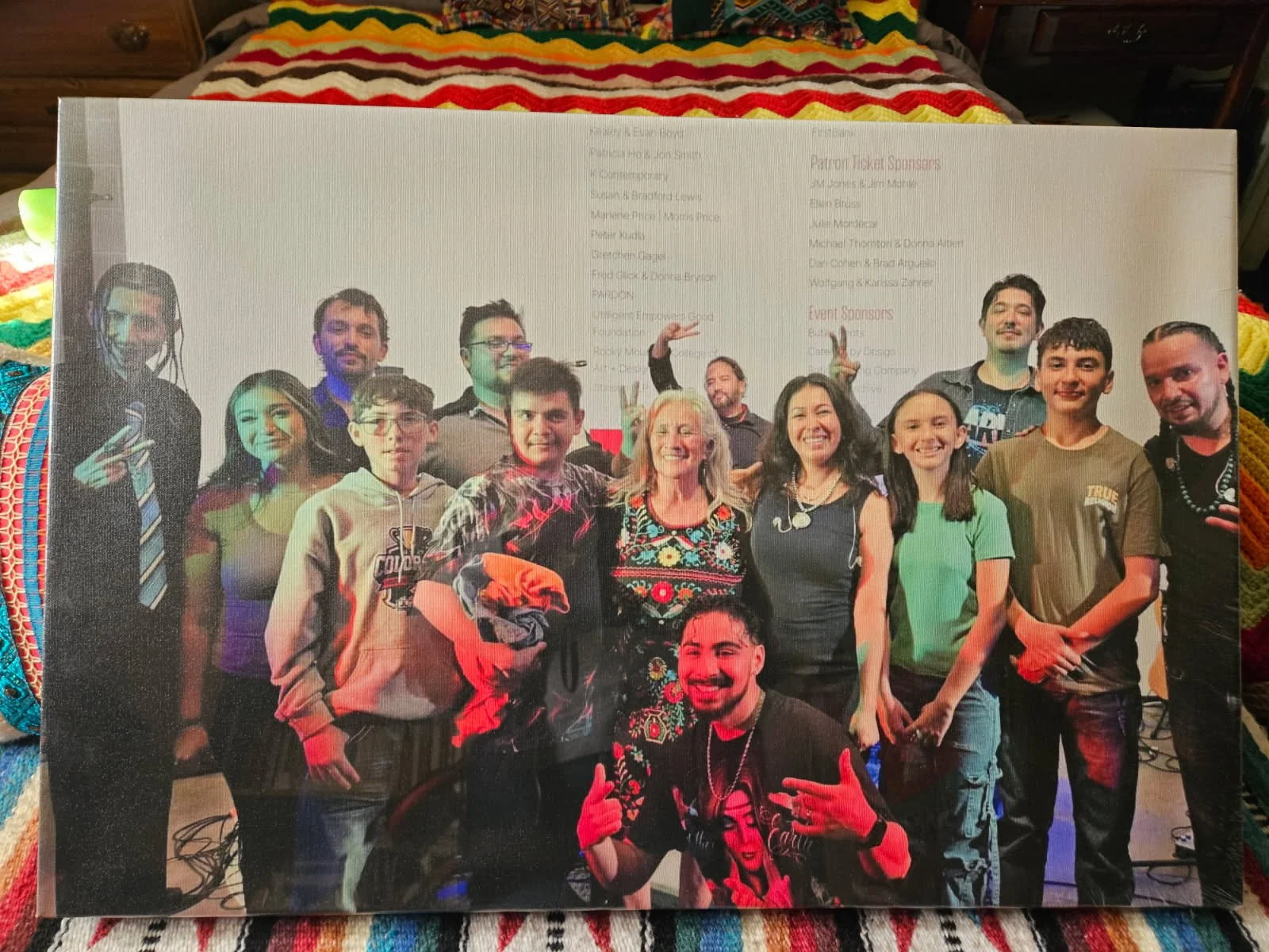 Group of people posing for a photo at an event, some making hand gestures, in front of a white backdrop with text.