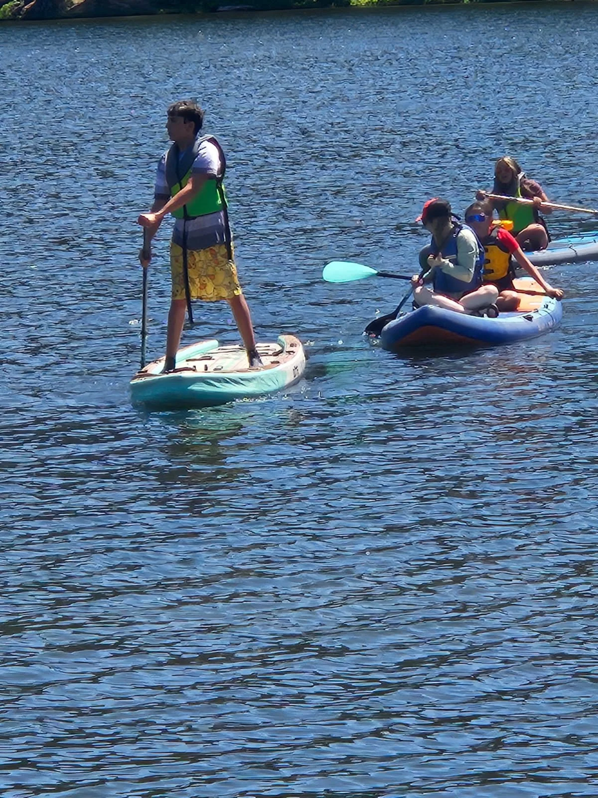 Two kids paddleboarding and kayaking on a lake on a sunny day.