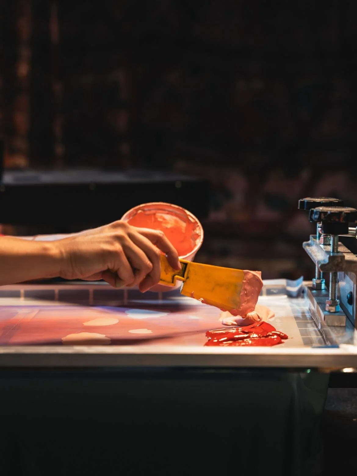 Person adding colored silk screen ink onto a printing surface for screen printing.