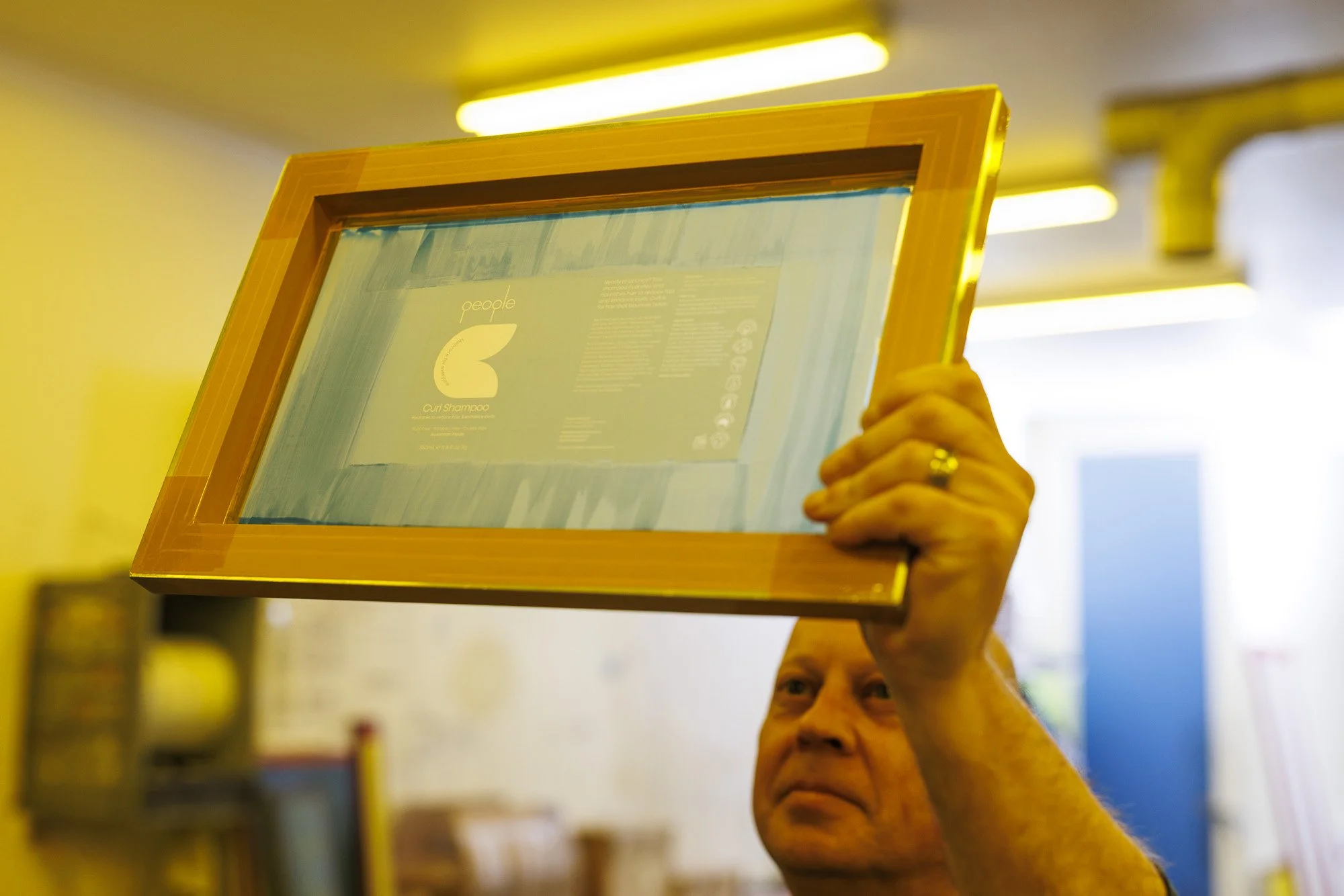 Man holding a framed, clear product display in a store, with bright yellow lighting overhead.