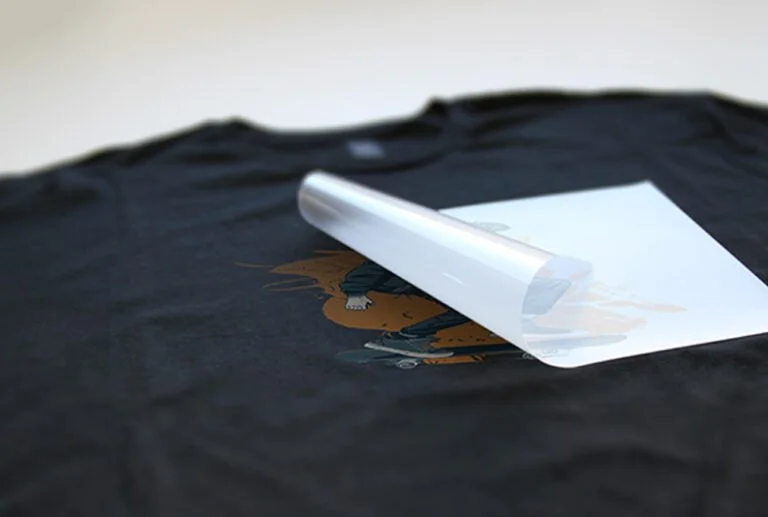 DTF adhesive powder applied on transfer film placed over a t-shirt before heat transfer process.