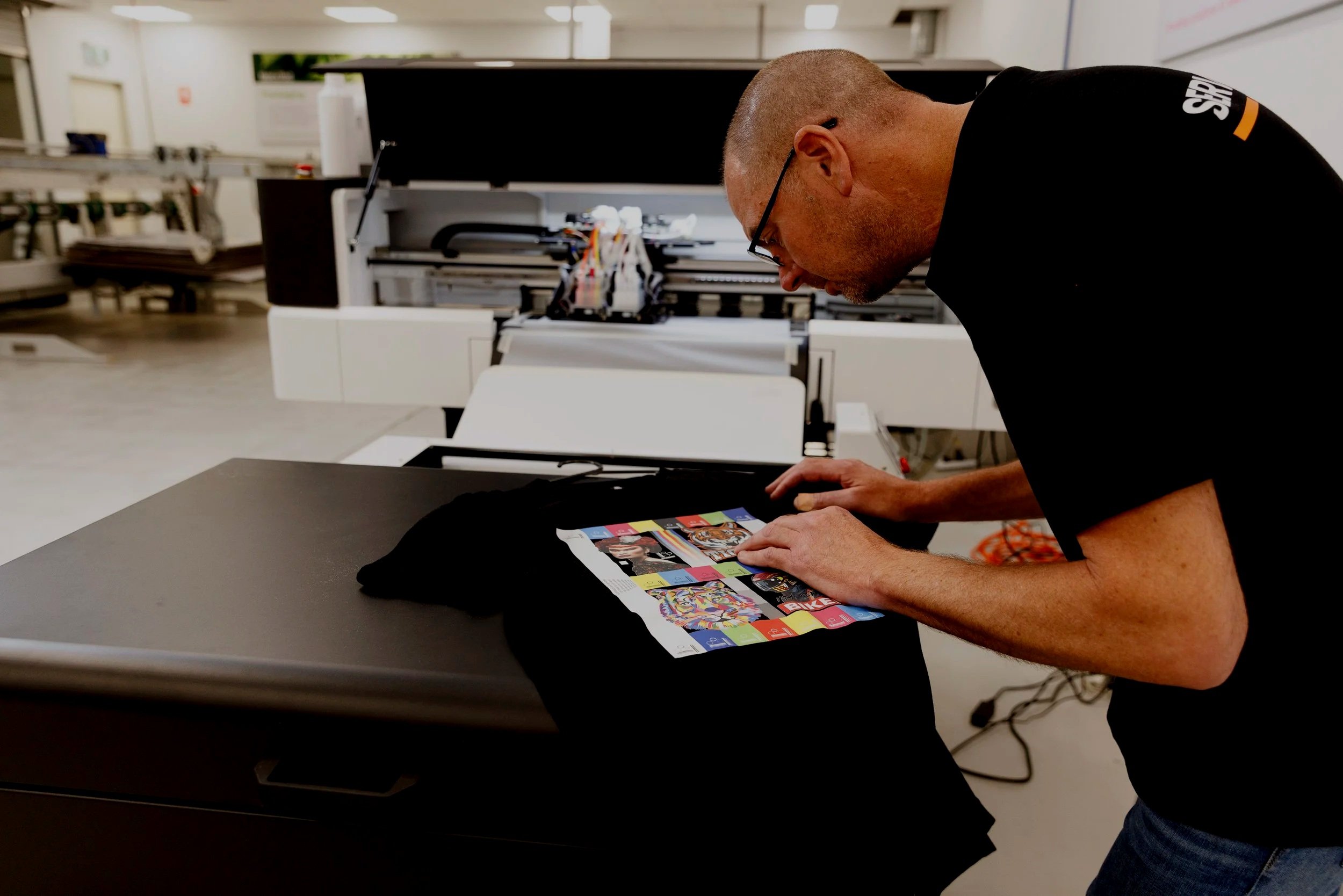 Operator inspecting a Direct-to-Film (DTF) printed transfer on a t-shirt in a professional textile printing facility