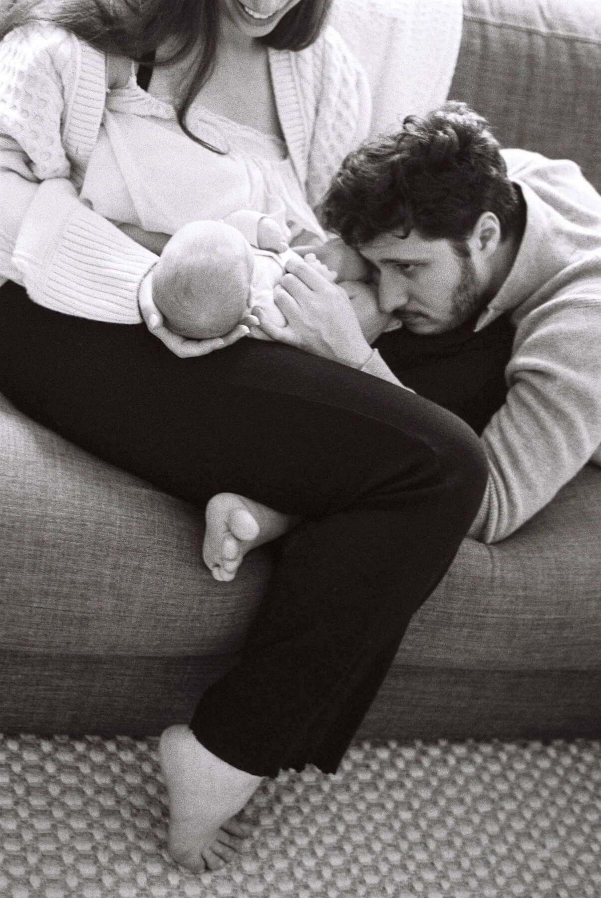A candid moment from a newborn photoshoot in Berlin: mom and dad cuddle their baby on a sofa