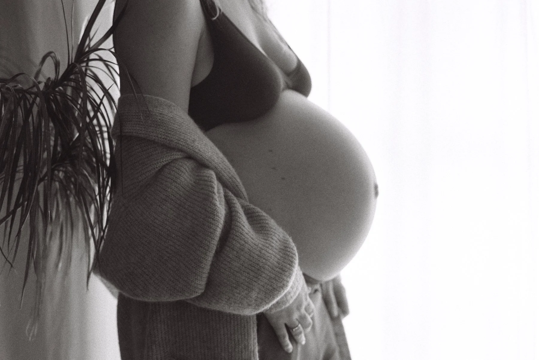 A black and white analog shot from a maternity session in Berlin: a pregnant woman's belly in front of a window