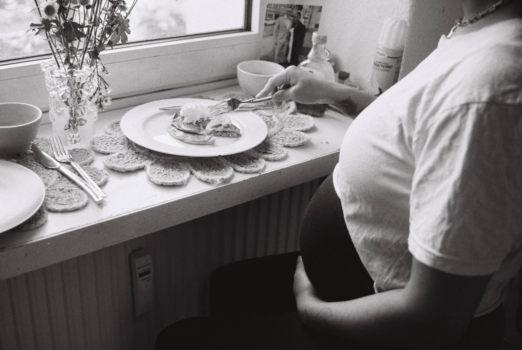 A pregnant woman sits at a windowsill eating pancakes: candid moment from a maternity photoshoot in Berlin