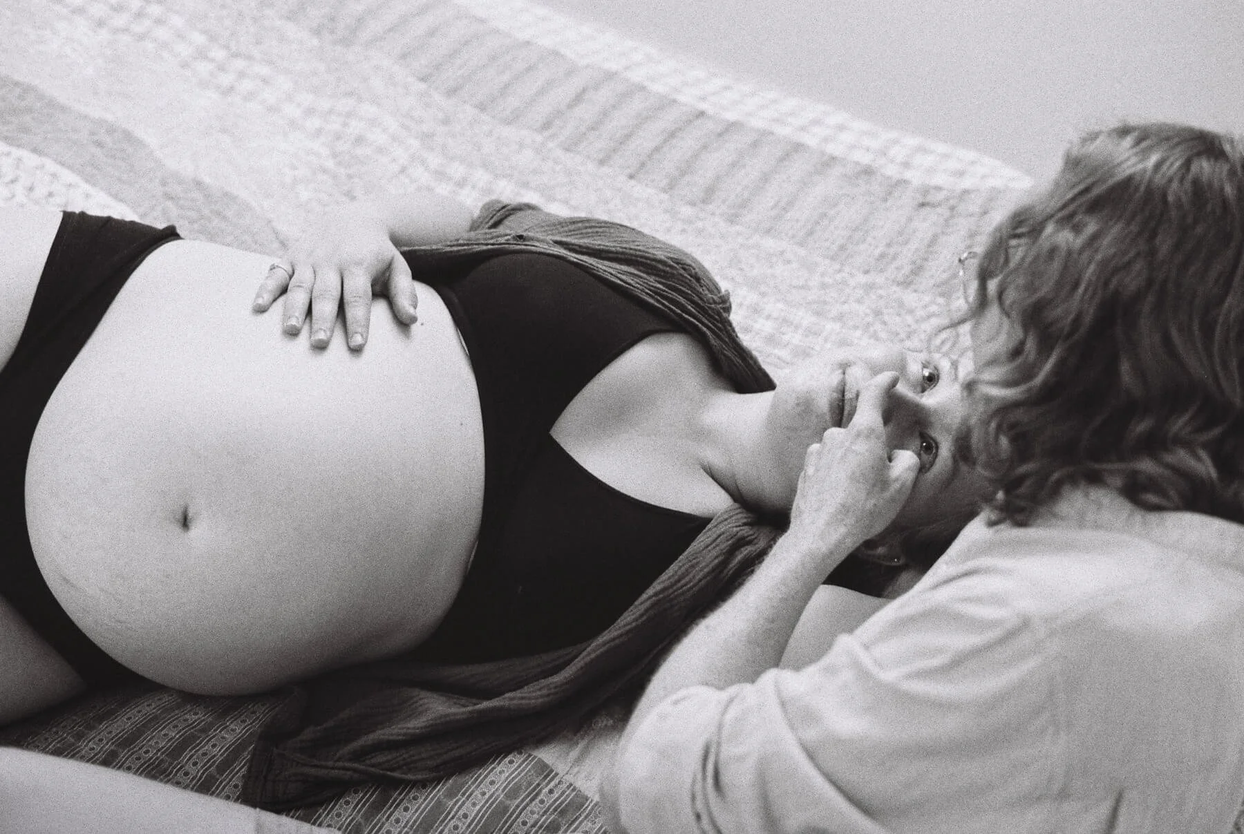 Inniger Moment bei einem Babybauchshooting in Potsdam: Eine schwangere Frau liegt lächelnd auf dem Bett, ihr Partner berührt sanft ihre Nase