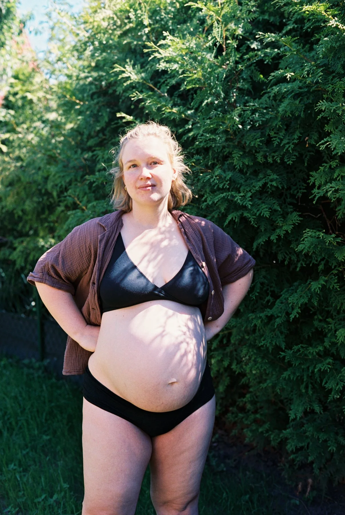 Pregnant woman in the garden, hands on her heaps - a moment from a maternity shoot in Berlin