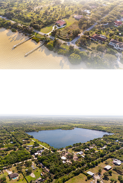 Aerial view of a waterfront area with docks and residential houses surrounded by trees and greenery, featuring a large pond and a grid of streets and homes.