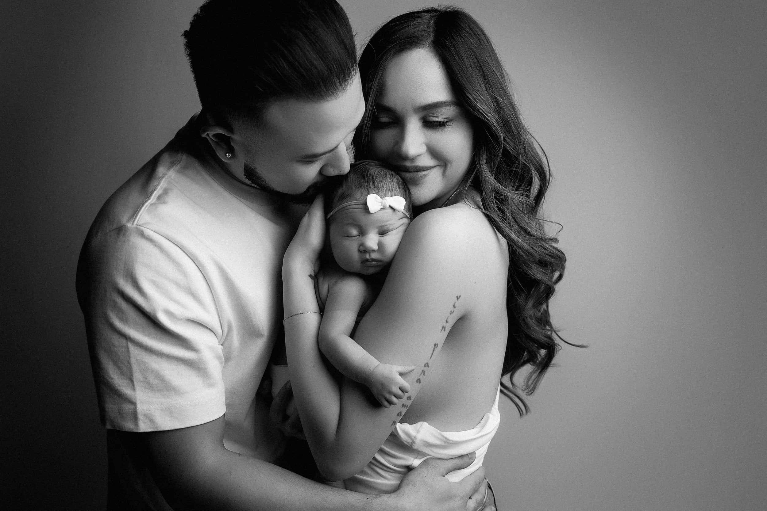 Black and white photo of a family with a man, woman, and baby, all embracing each other closely with happy expressions.