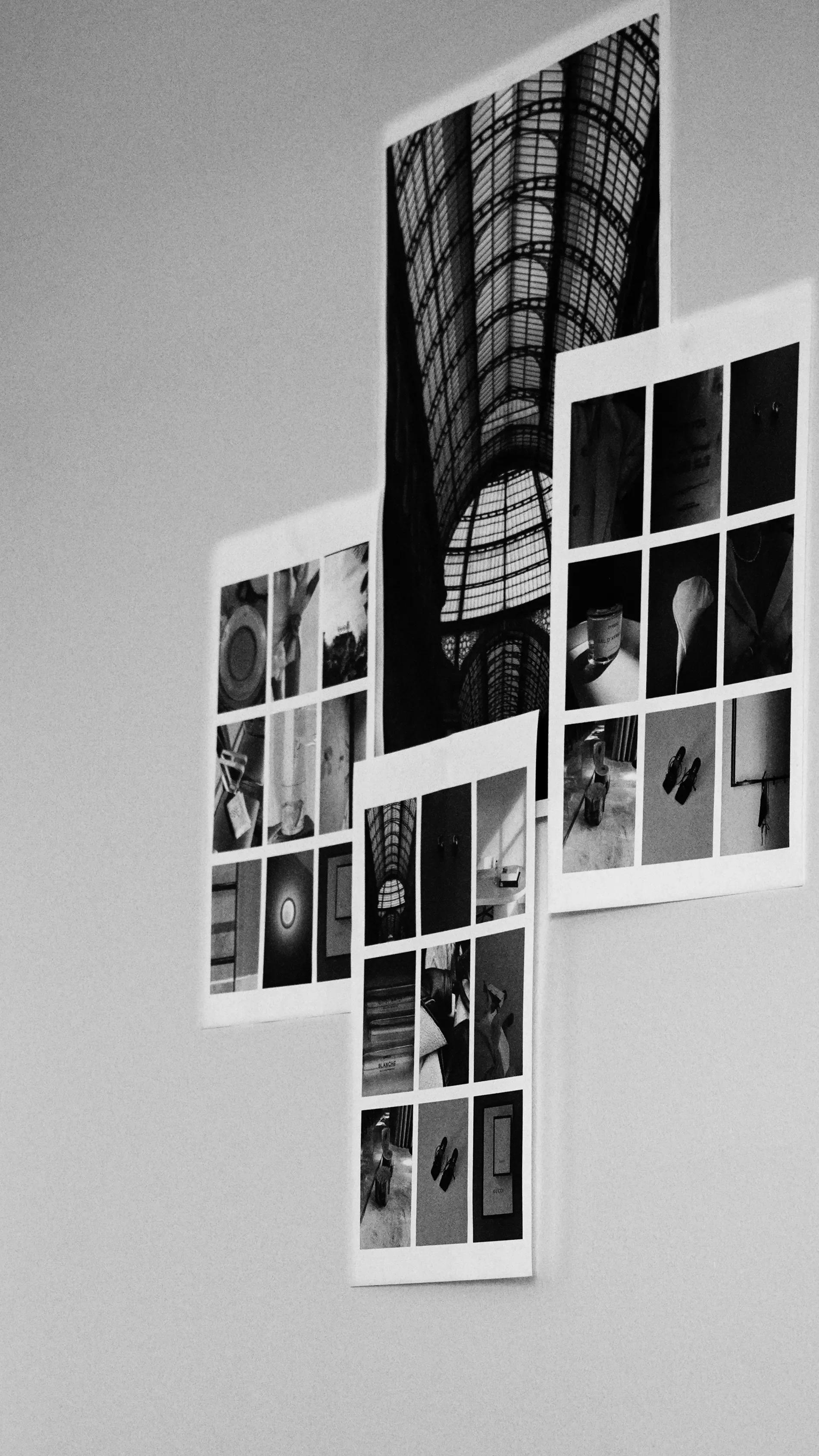 Black and white photo of indoor wall with two photo collages, one tall and narrow, one wide and horizontal, showing various images including a building interior, shoes, and objects.