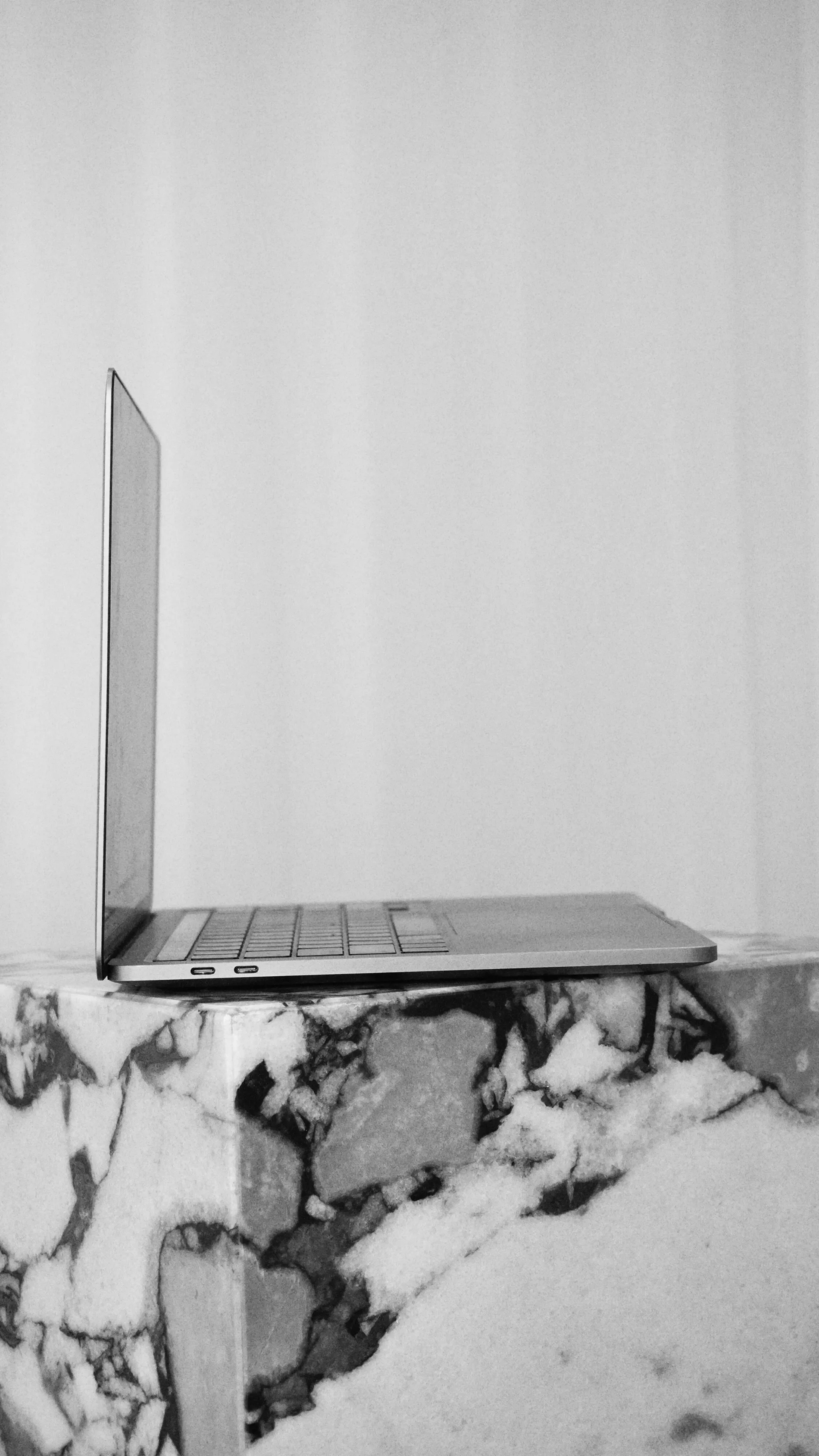 A laptop computer with an open silver case placed on a marble surface with a white wall in the background.
