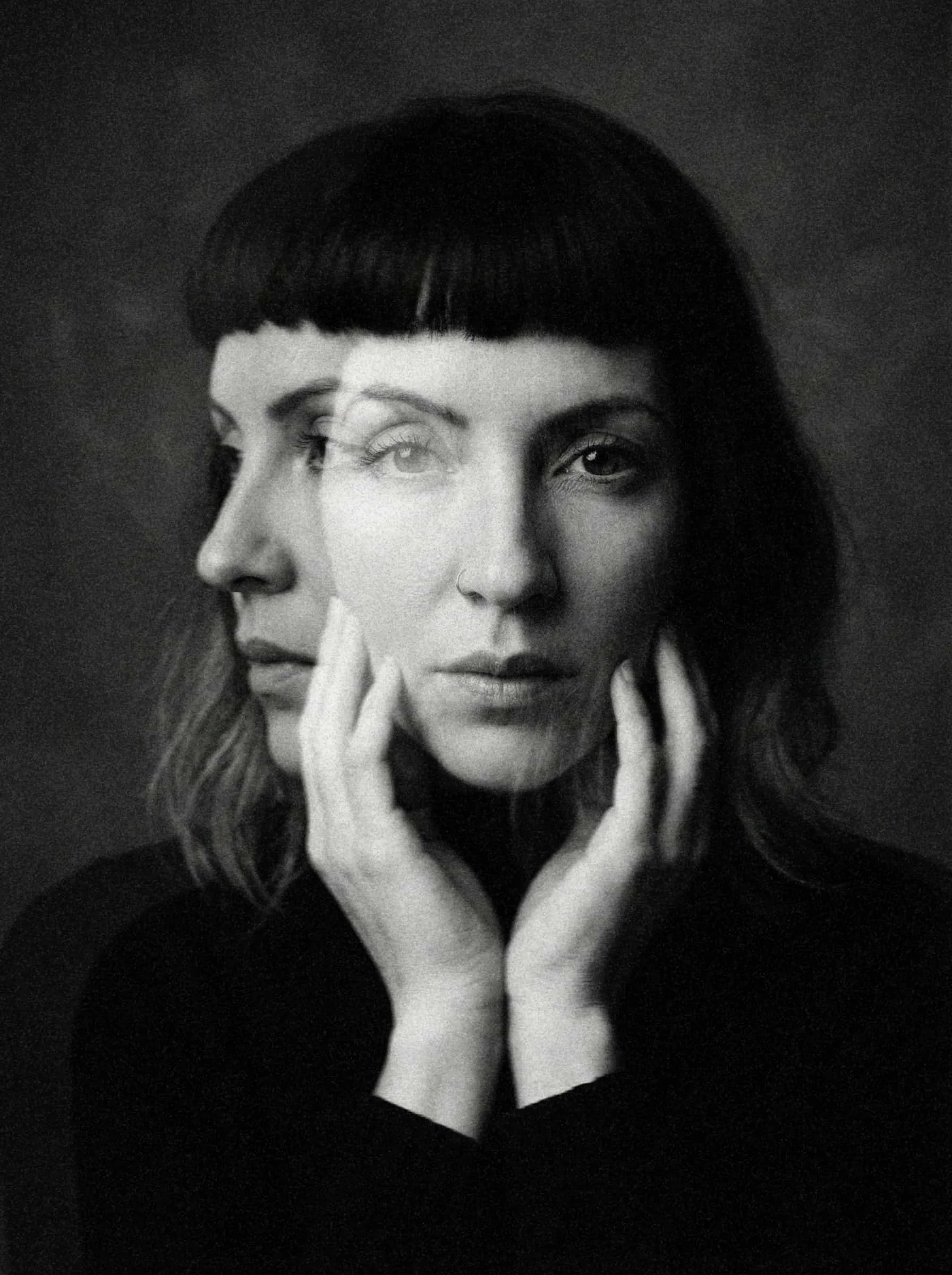 Black and white photo of a woman with short dark hair, bangs, and a nose piercing. She has a serious expression, and her face is partially obscured with multiple overlayed images. Her hand touches her chin and cheek.
