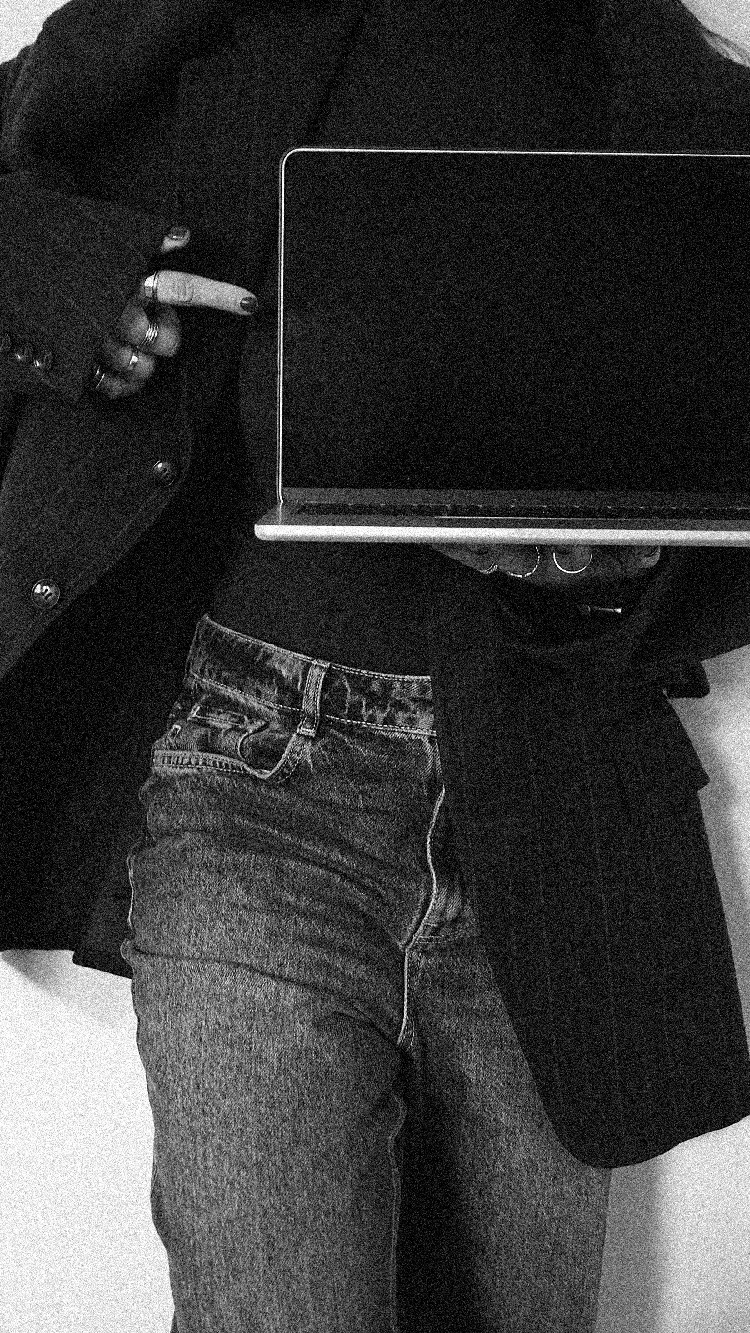Person wearing dark clothing and denim jeans, holding a laptop, with their hand giving a peace sign