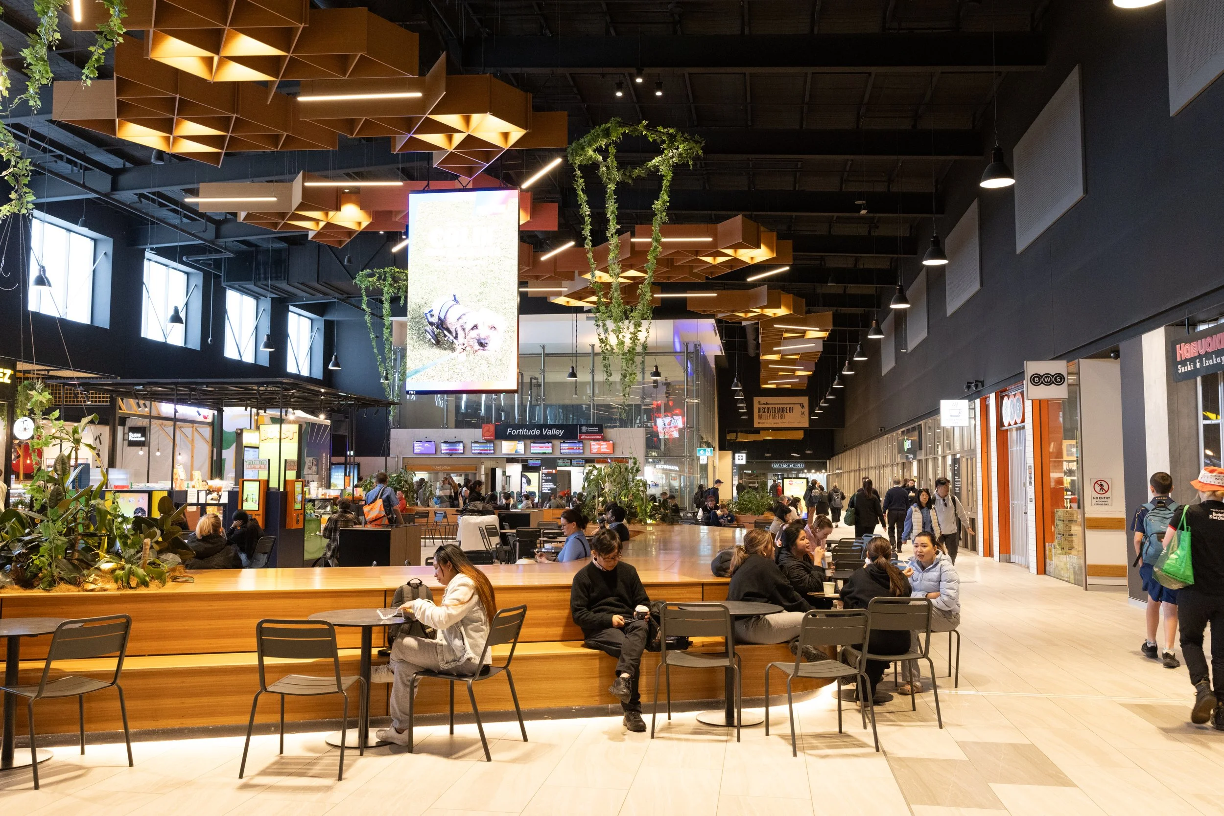 People sitting and walking inside a modern shopping mall with food stalls and shops.