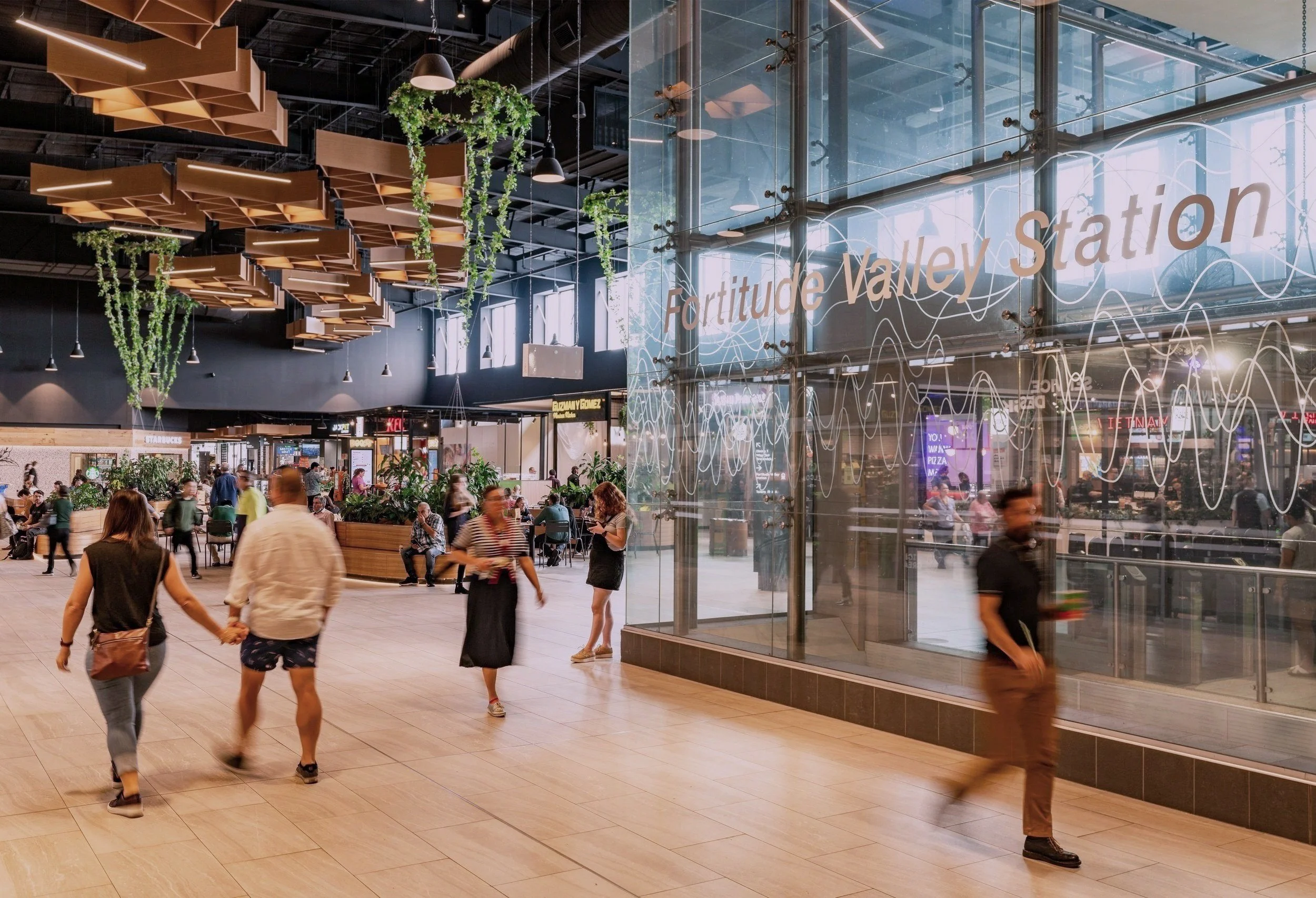 People walking through the spacious interior of Fortitude Valley Station with modern decor and hanging plants.