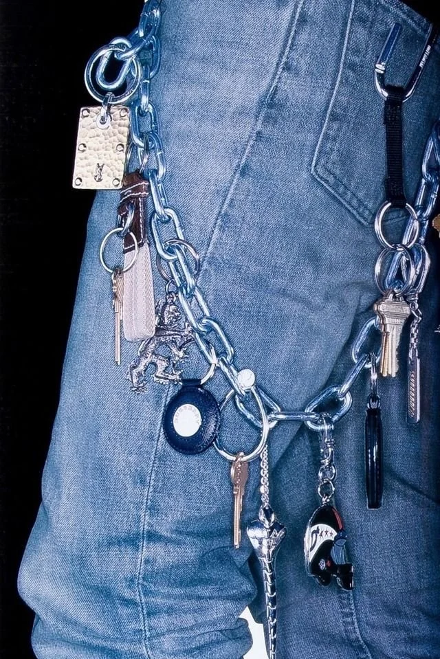 Person wearing blue jeans with multiple keychains and accessories hanging from a large chain around their waist.