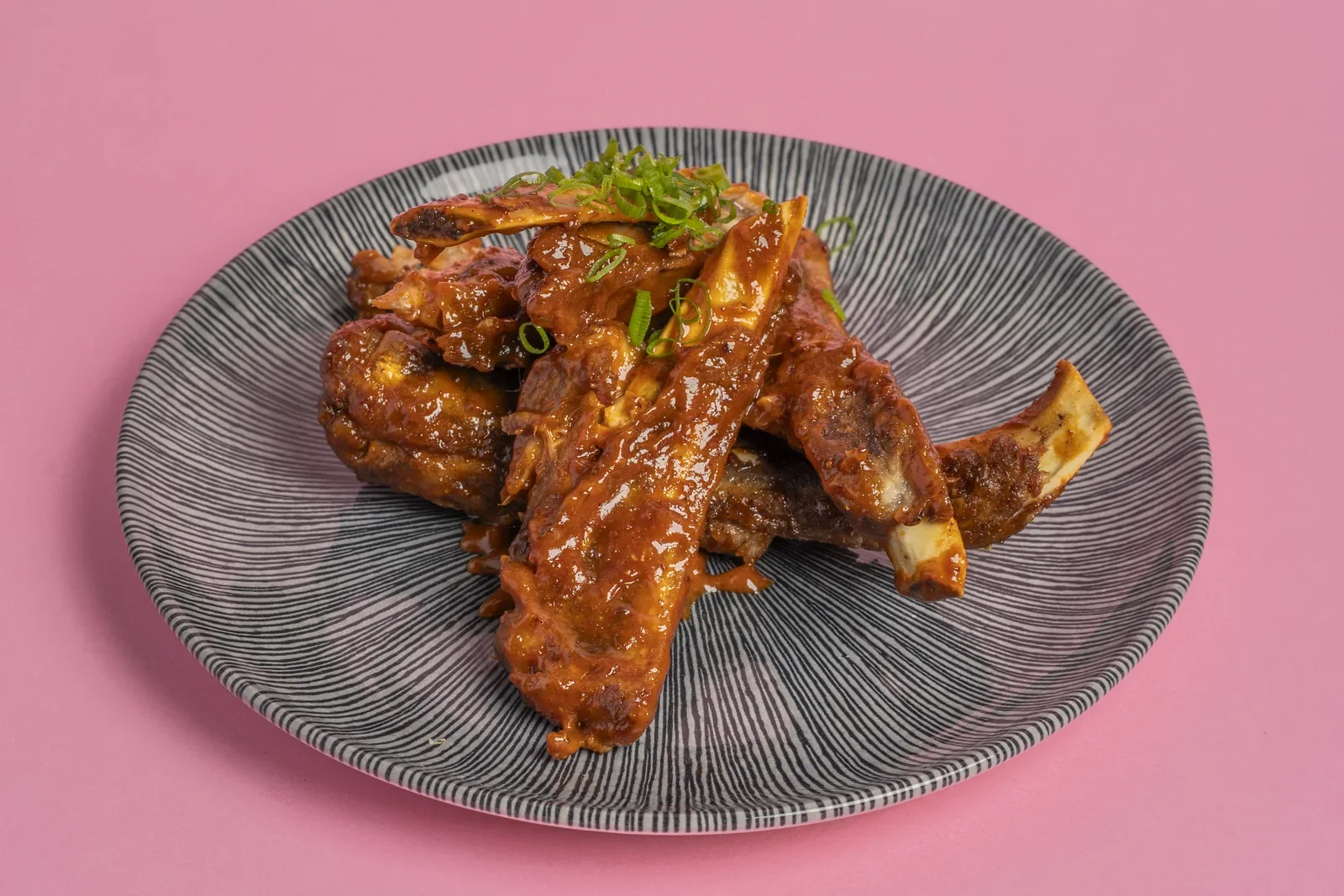 Glazed wings with green garnish on a dark plate.
