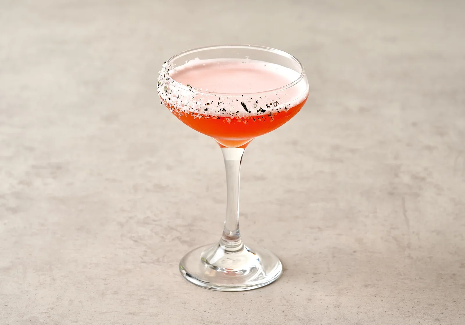 Pink cocktail in a coupe glass on a pale tabletop.