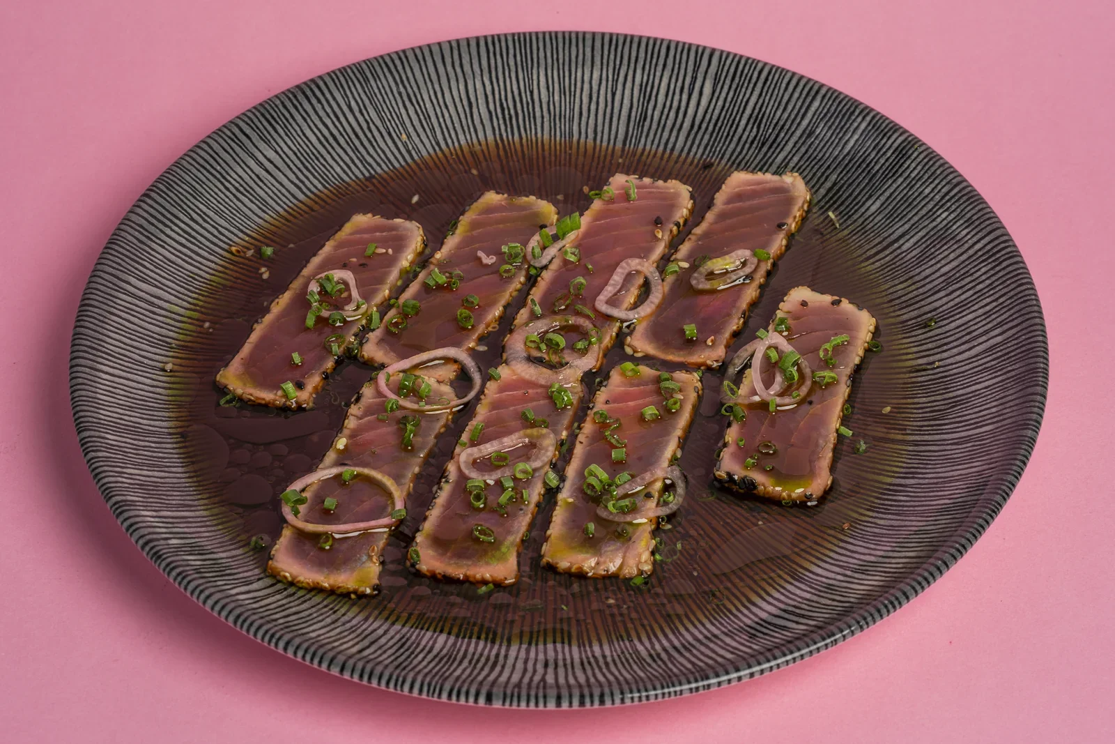 Slices of seared fish with green garnish on a dark plate.
