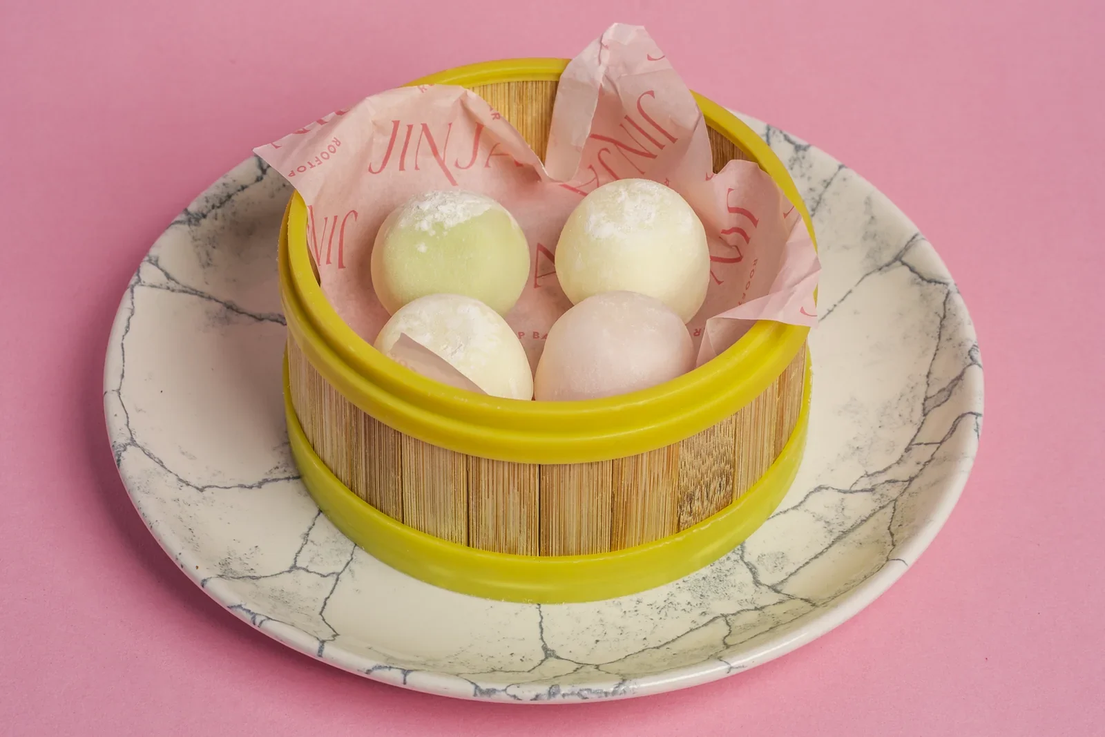 Pastel-coloured round desserts in a bamboo steamer basket.