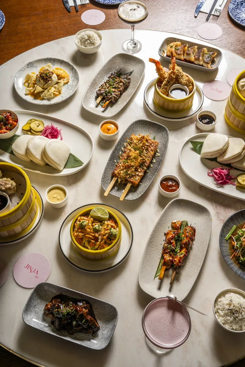Overhead view of a Jinja table with steamer baskets, sharing plates and cocktails.