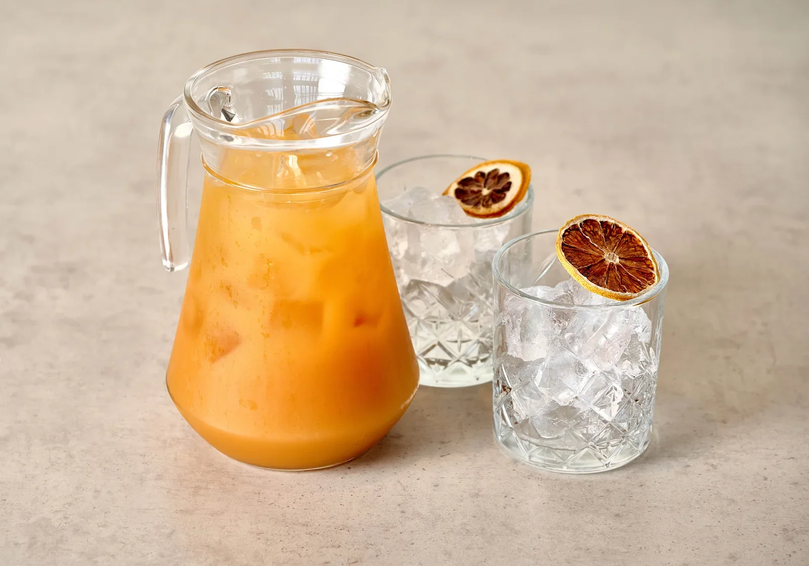 Orange cocktail jug beside two glasses with dried citrus garnishes.