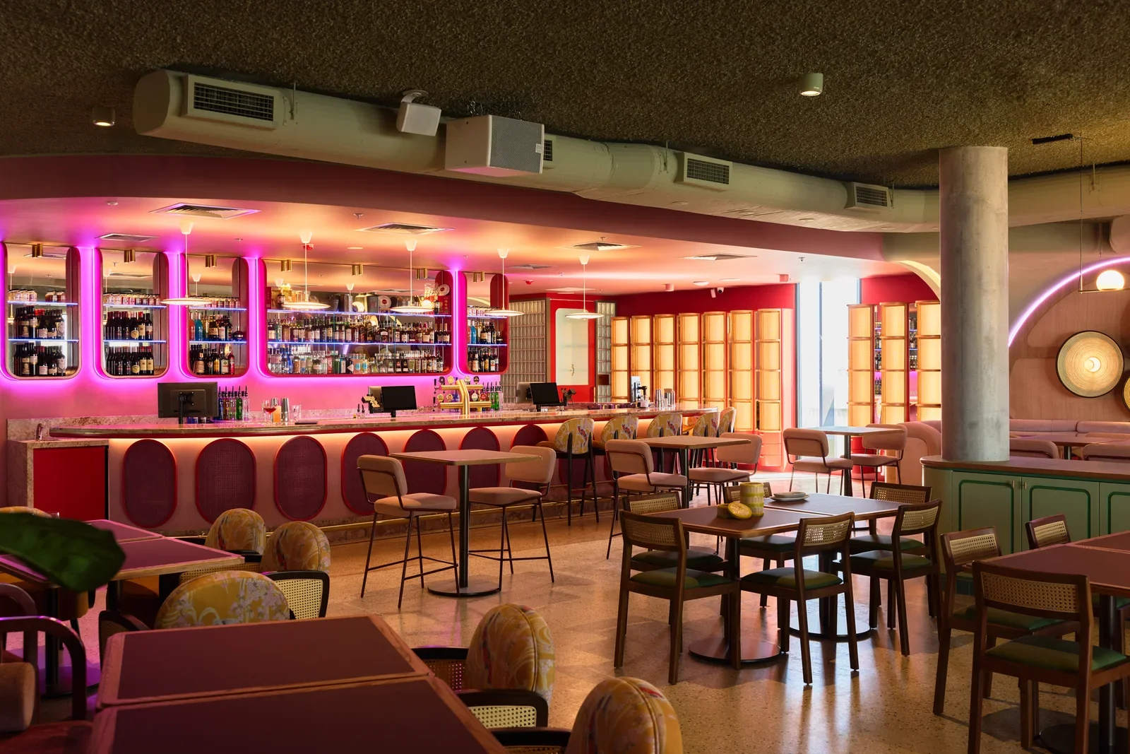 Jinja bar with pink-lit bottle shelves, curved stools and dining tables.