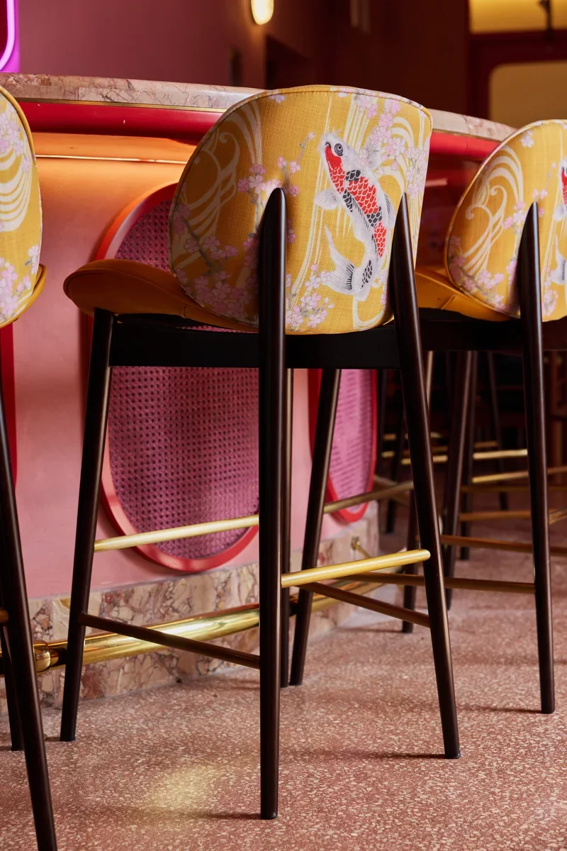 Patterned yellow bar stools beside Jinja’s pink-lit curved bar.