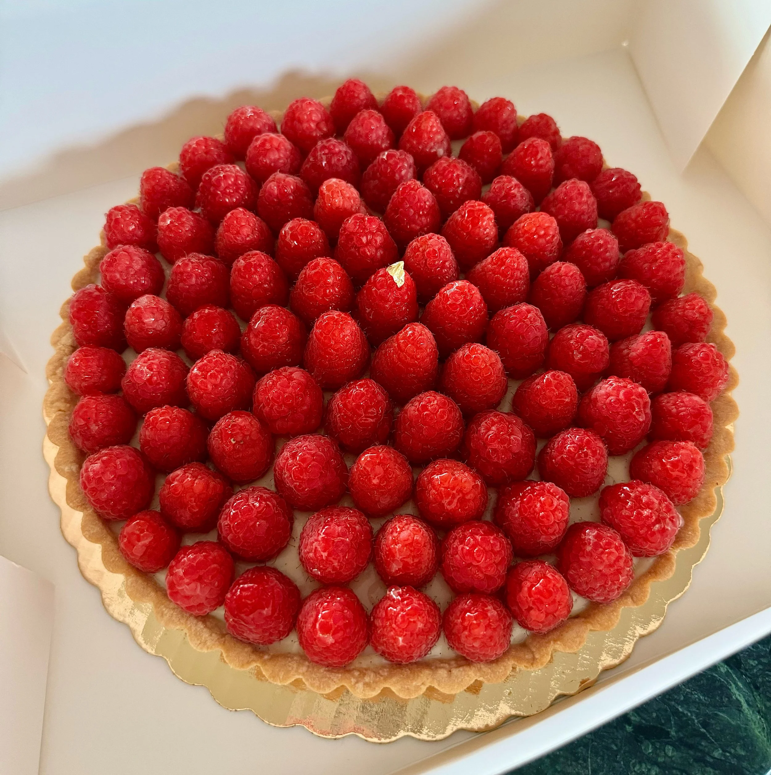 Raspberry tart with fresh raspberries on top, in a gold-colored tart crust