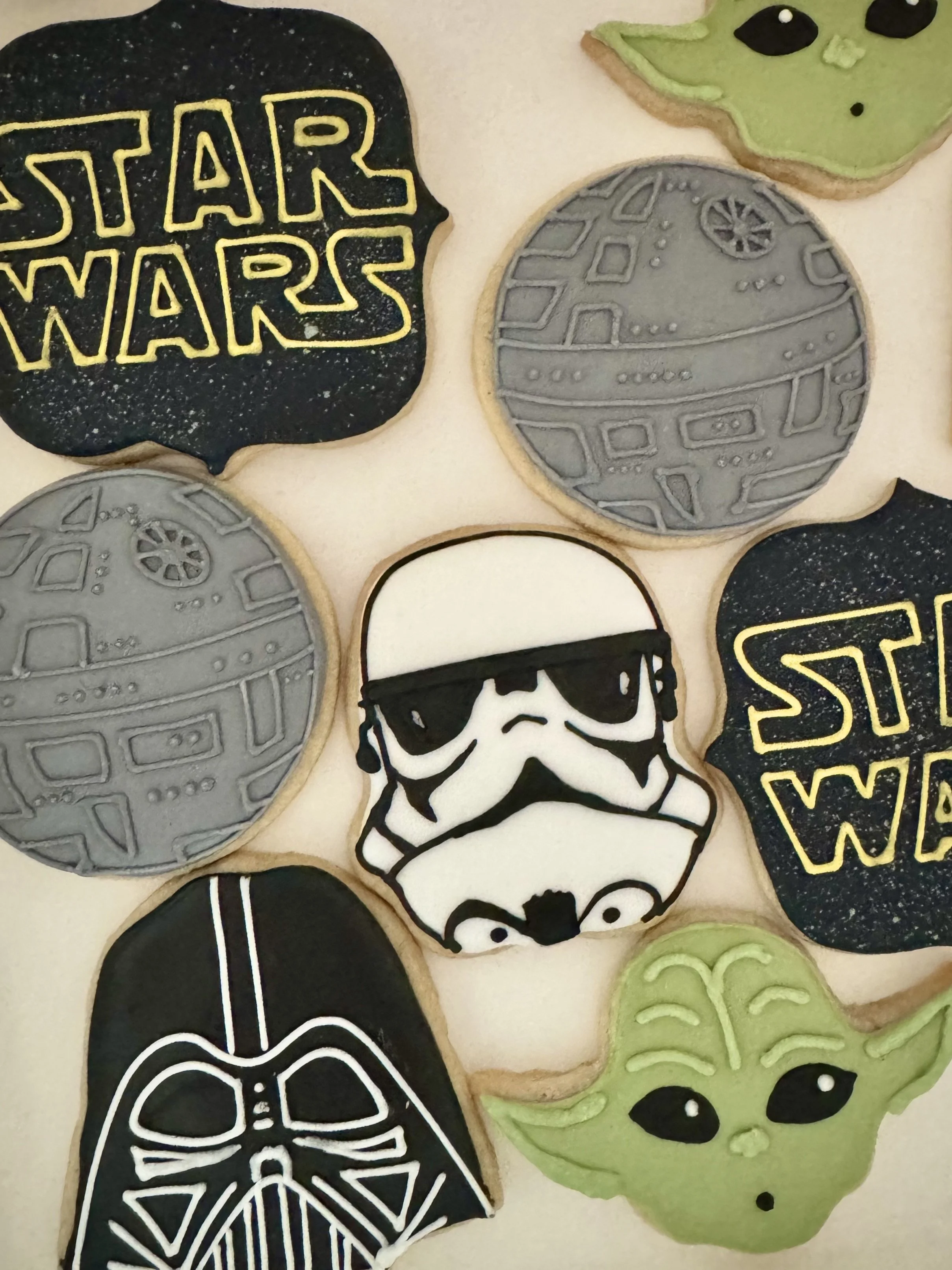 Star Wars themed decorated cookies, including a black Darth Vader mask, Yoda's face, a Stormtrooper, and two gray Death Star cookies.