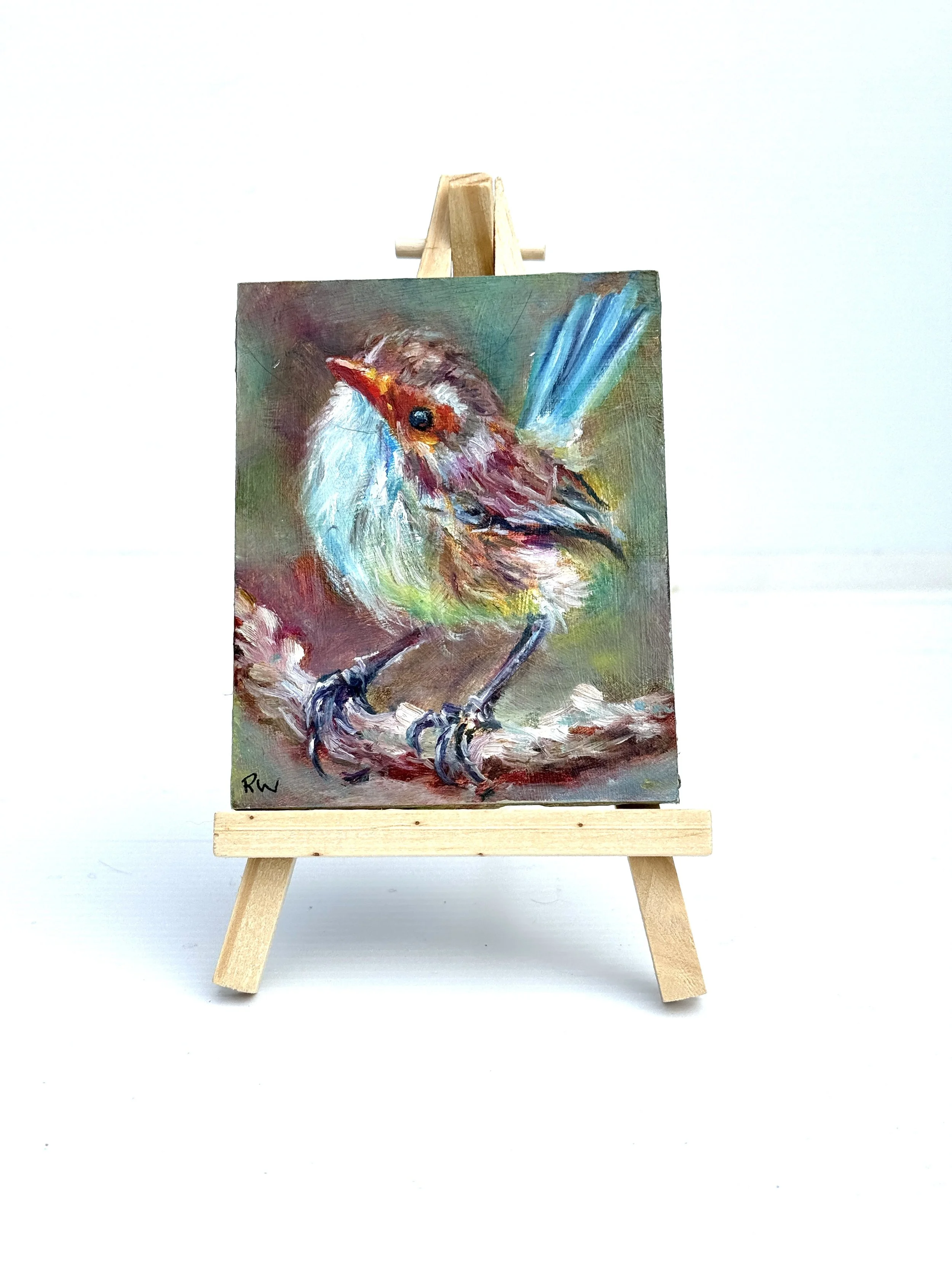 Mini oil painting of a colourful blue wren on a branch, on a wooden easel.