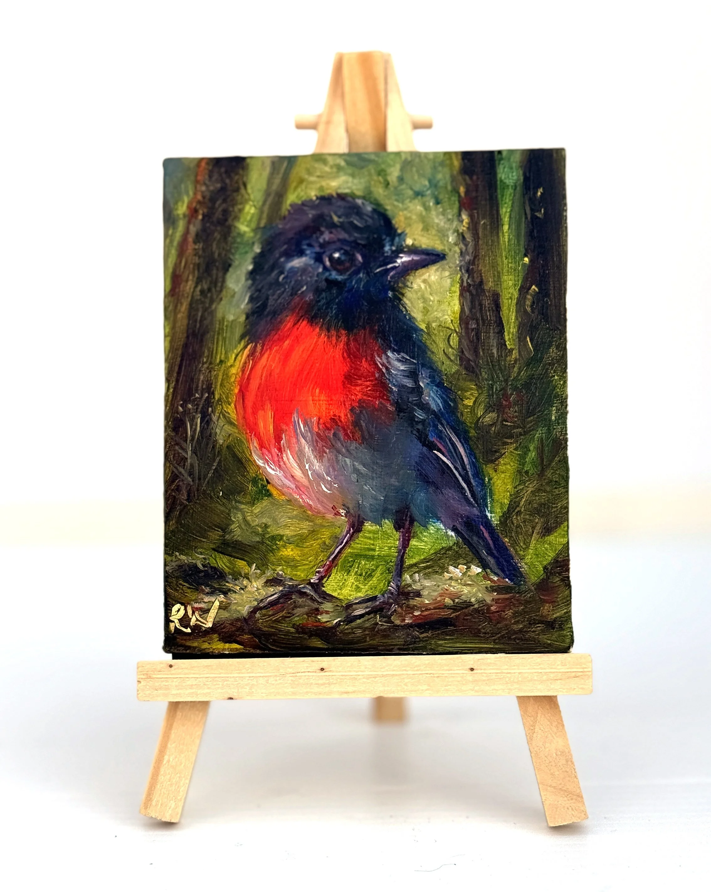 Mini oil painting of a red-chested robin standing on a branch, on a wooden easel.