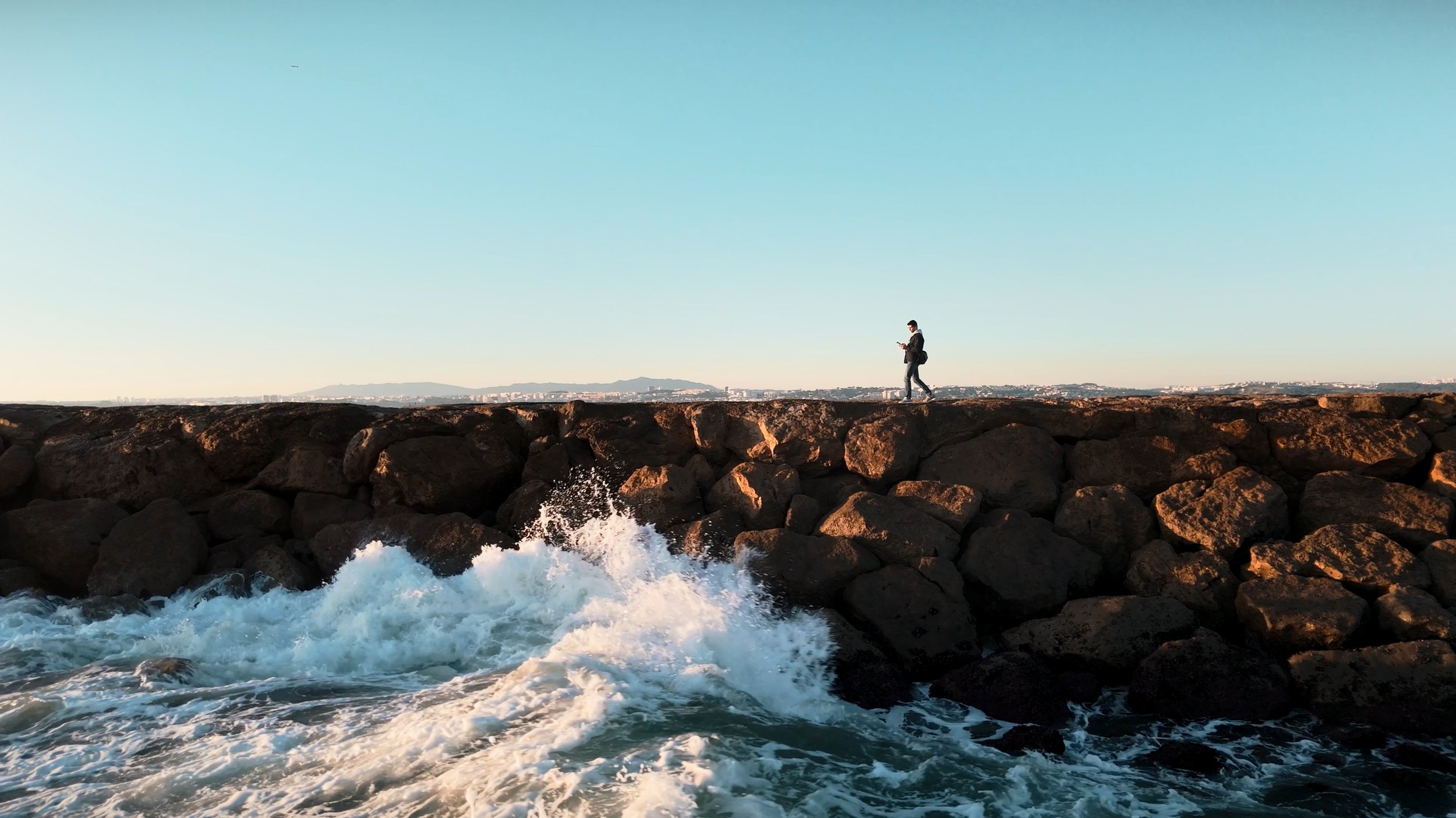 Man walking along a rocky breakwater with crashing waves, lifestyle shot