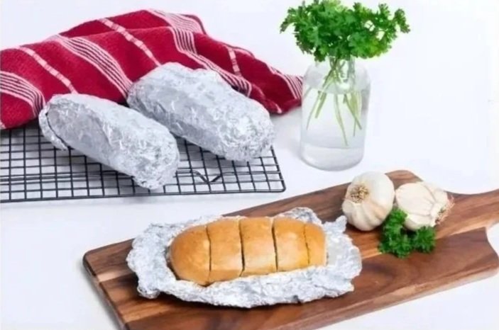 Shop Preview: Sliced garlic bread on foil, whole garlic bulbs, parsley, and bread loaves on a rack with a red towel and parsley in a jar.