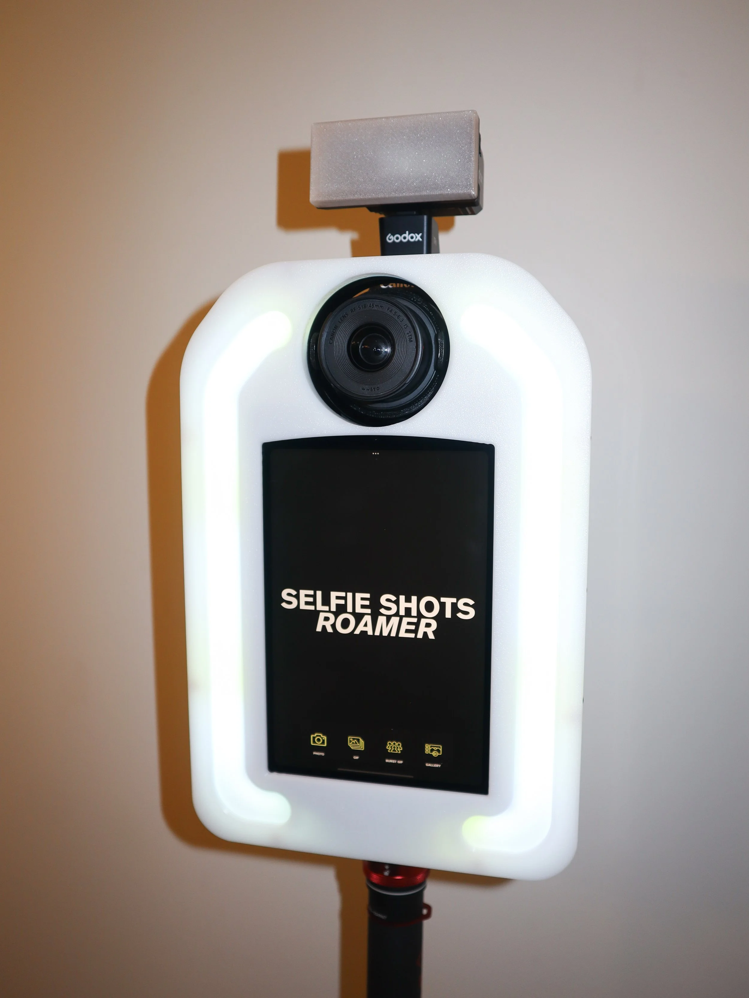 A selfie camera booth with a display screen that reads 'SELFIE SHOTS ROAMER' and icons for camera, gallery, settings, and print.