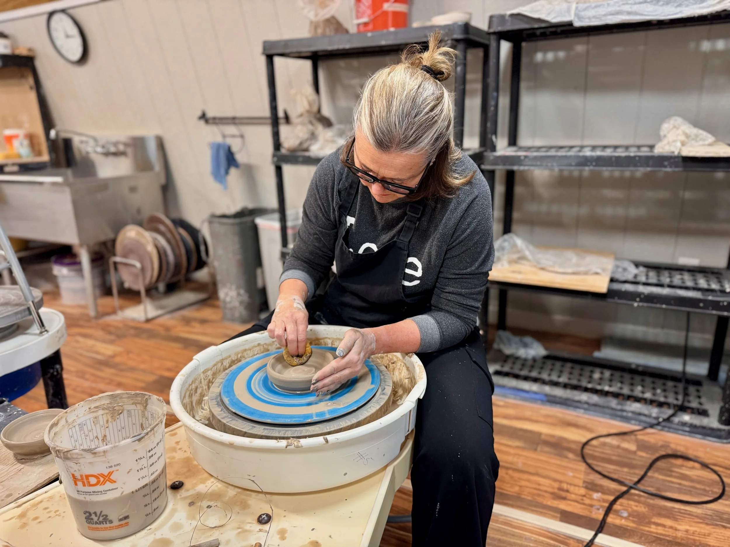 Woman shaping clay on a pottery wheel in a ceramics studio.